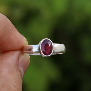 Pode incluir: Um anel de prata com uma pedra oval vermelha.