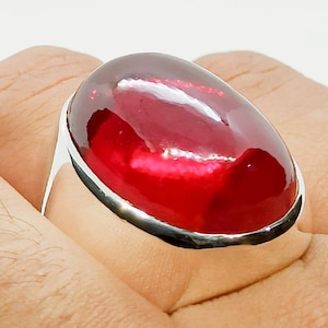 Op de afbeelding: Een zilveren ring met een grote, ovale, rode edelsteen.