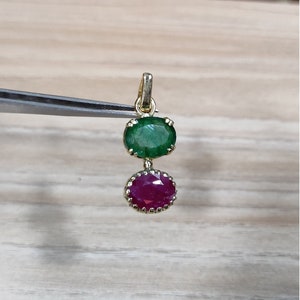 May include: A gold pendant with a green emerald gemstone and a red ruby gemstone.