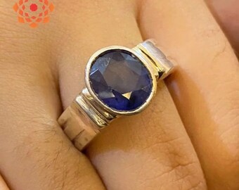 May include: A silver ring with a large, oval-cut, deep blue gemstone. The ring has a simple, modern design with a thick band and a bezel setting that holds the stone securely. The gemstone is the focal point.