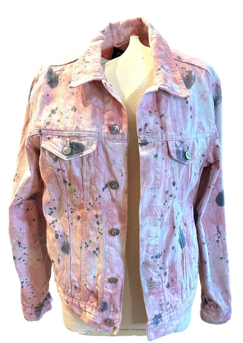 Op de afbeelding: Een roze denim jack met een splatter paint design in zwart en grijs.