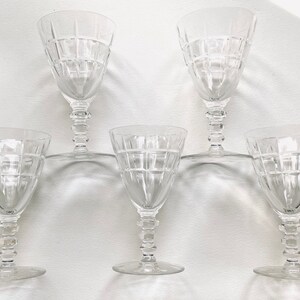 Może przedstawiać: Zestaw sześciu przezroczystych szklanek do wina z geometrycznym wzorem. Szklanki są ułożone w półkole na białym tle.