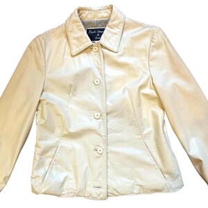 May include: A cream-colored leather jacket with a button-up front and a collar. The jacket has a label that reads "First Avenue in Paris".