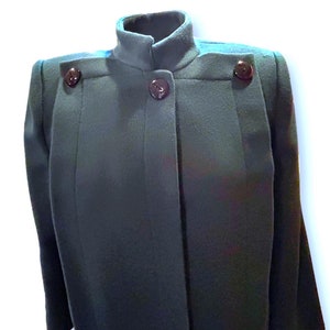 May include: A dark green, collared jacket with a single button closure and two additional buttons on the shoulders. The jacket has a simple, tailored design.