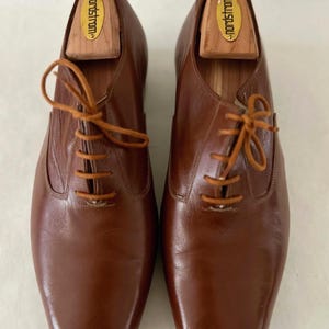 May include: A pair of brown leather dress shoes with matching laces. The shoes have a classic design with a square toe and are shown with wooden shoe trees inside. The shoe trees are branded with the word "nordstrom".