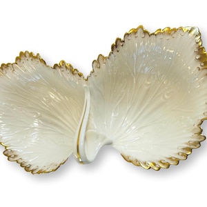 May include: A white, leaf-shaped serving dish with a gold-colored trim. The dish is divided into two sections and has a delicate, veined pattern. The edges are scalloped, adding a touch of elegance to this decorative piece.