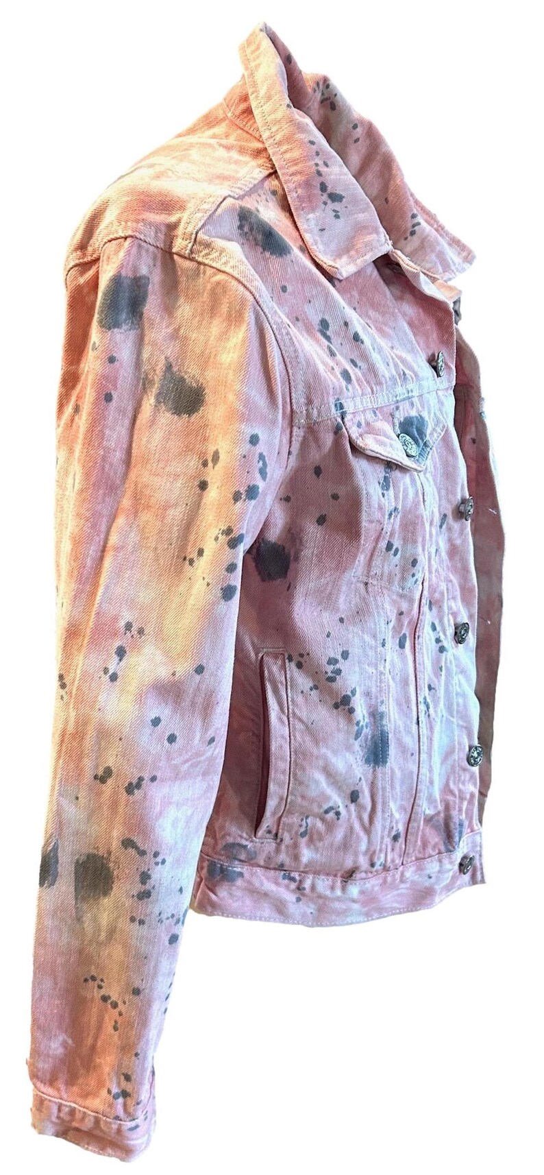Op de afbeelding: Een roze denim jack met zwarte verfspatten. Het jack heeft een klassieke denim jack stijl met een knoopsluiting en twee zakken.