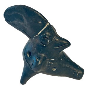 May include: A dark charcoal-colored ceramic ocarina shaped like a stylized bird head. The instrument features a prominent curved crest, a pointed beak, circular eyes, and multiple small finger holes positioned along the side and base surface.