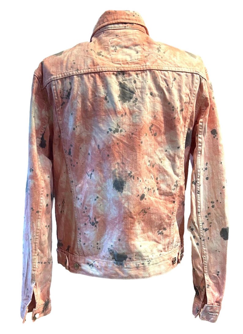 Op de afbeelding: Een roze denim jack met een splatter paint design in grijstinten en wit.