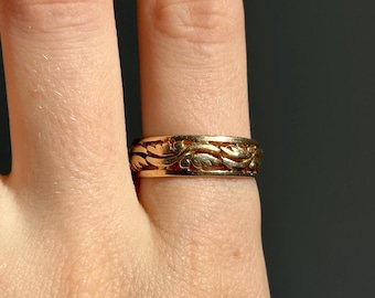 May include: A gold band ring with an intricate, swirling design.
