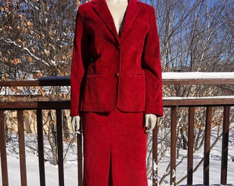 Puede incluir: Un traje de falda de pana roja con una chaqueta y una falda. El traje está en un maniquí y está de pie sobre una superficie nevada.