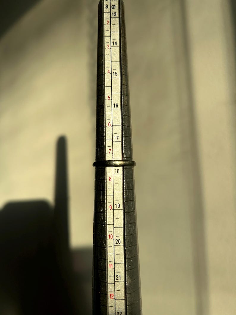 K&ouml;nnte beinhalten: Ein Metall-Ringma&szlig; mit Markierungen von Gr&ouml;&szlig;e 13 bis 22. Der Ringma&szlig; wird verwendet, um die richtige Ringgr&ouml;&szlig;e zu bestimmen.