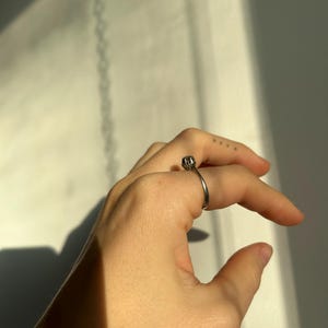 K&ouml;nnte beinhalten: Ein silberner Ring mit einem strukturierten Design auf der Band. Der Ring wird am Mittelfinger einer Hand getragen.