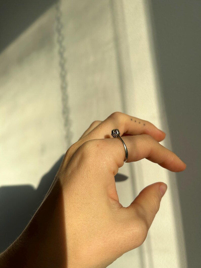 K&ouml;nnte beinhalten: Ein silberner Ring mit einem strukturierten Design auf der Band. Der Ring wird am Mittelfinger einer Hand getragen.