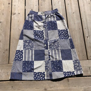 Peut inclure: Une jupe en patchwork bleu et blanc avec une fermeture boutonnée. La jupe présente une variété de motifs, notamment floraux, géométriques et à pois.