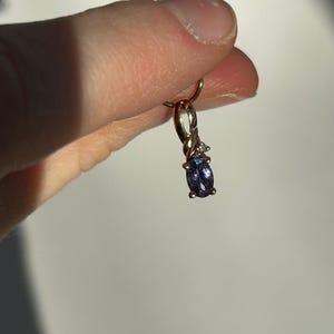 Pode incluir: Um pingente de ouro com uma pequena pedra preciosa oval azul escuro e duas pequenas pedras preciosas brancas. O pingente &eacute; suspenso por um la&ccedil;o de ouro.