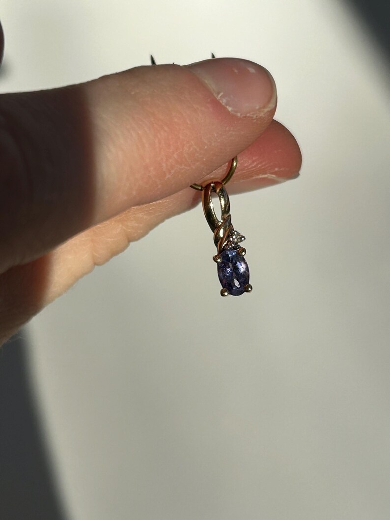 Pode incluir: Um pingente de ouro com uma pequena pedra preciosa oval azul escuro e duas pequenas pedras preciosas brancas. O pingente &eacute; suspenso por um la&ccedil;o de ouro.