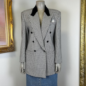 May include: A black and white houndstooth blazer with a black velvet collar and double-breasted button closure. The blazer has a small pocket square and is displayed on a mannequin. The blazer is paired with a denim skirt.