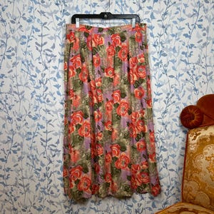 May include: A long, flowing skirt with a floral print featuring large red roses on a purple background. The skirt has a gathered waist and is made of a lightweight fabric.