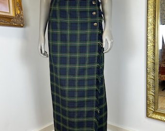 May include: A long, plaid skirt in navy blue and green, featuring a wrap design with decorative buttons and fringe trim. The skirt is displayed on a mannequin, showcasing its full length and style.