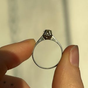 K&ouml;nnte beinhalten: Ein silberner Ring mit einem einzigen runden Edelstein, der in einer Krappenfassung sitzt.