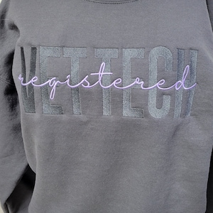 May include: A dark gray sweatshirt with the text "VET TECH registered" embroidered in black and purple.