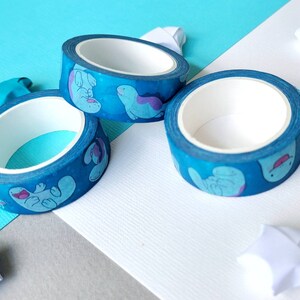 May include: Three rolls of blue washi tape with a white background. The tape has a pattern of cartoon sea creatures in shades of blue and purple.