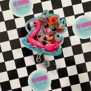 May include: A badge reel featuring a cartoon Highland cow wearing sunglasses and a floral crown, relaxing on a pink flamingo float. The cow is holding a drink. The badge reel has a clear plastic clip and the text "SG Designs By Danielle" is on a round sticker.
