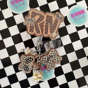 Pode incluir: Um porta-crachá com as letras "RN" em um design de estampa de leopardo, acentuado com glitter e um laço. O porta-crachá inclui um pingente com uma borboleta e um laço xadrez. O fundo é um padrão xadrez em preto e branco.