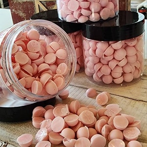 May include: Several clear plastic jars filled with light pink, half-sphere shaped candies. Some candies are spilled out of a jar onto a wooden surface. The jars have black lids. The image suggests a food or confectionery product.