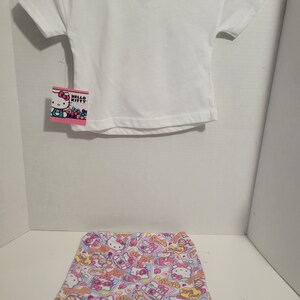 May include: A white short-sleeved t-shirt with a Hello Kitty tag and a pair of white and pink shorts with a Hello Kitty print.