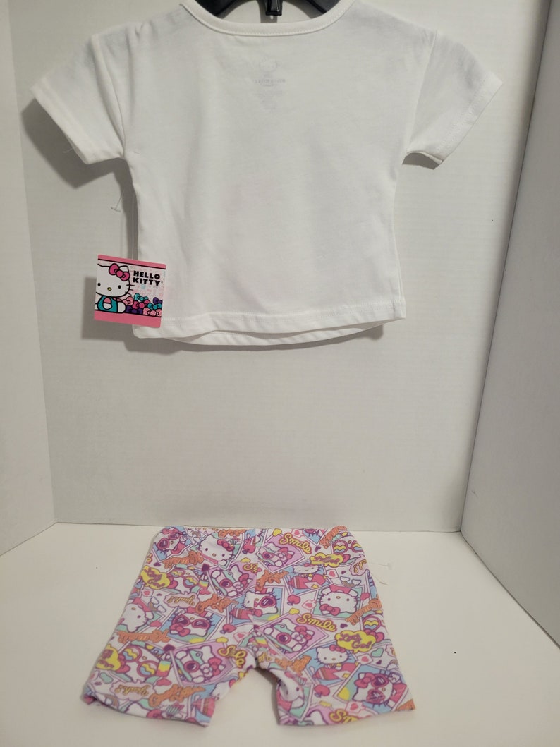 May include: A white short-sleeved t-shirt with a Hello Kitty tag and a pair of white and pink shorts with a Hello Kitty print.