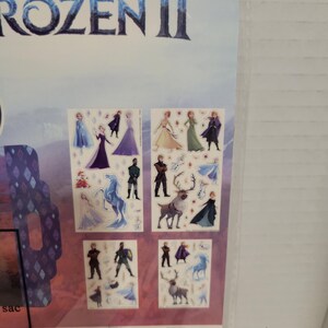 May include: A set of Frozen II stickers featuring characters from the movie, including Elsa, Anna, Kristoff, Olaf, and Sven. The stickers are on a white background with a blue and purple border.