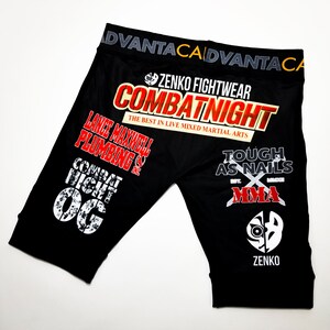 May include: Black athletic shorts with a variety of colorful patches and logos, including "Combat Night", "Zenko Fightwear", "Tough as Nails MMA", and "Lance Maxwell Plumbing".