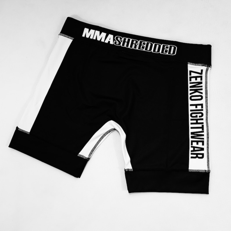 May include: Black athletic shorts with white side panels and the text "MMASHREDDED" and "ZENKO FIGHTWEAR" printed on the sides.