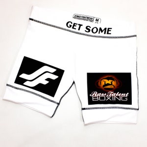 May include: White athletic shorts with black stitching and a black and white logo on the left leg. The right leg has a black patch with a cartoon monkey and the text "Raw Talent Boxing" in white.