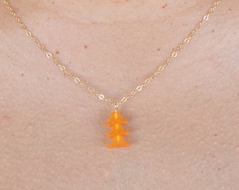 Puede incluir: Un collar de cadena dorada con un pequeño colgante naranja en forma de pagoda de tres niveles.