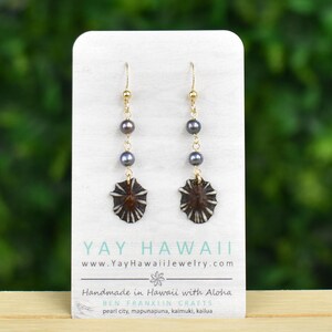 Könnte beinhalten: Goldfarbene Ohrringe mit dunkelgrauen Perlen und braunen, sternförmigen Anhängern. Die Ohrringe werden auf einer weißen Karte mit dem Text "YAY HAWAII" und "Handmade in Hawaii with Aloha" präsentiert.