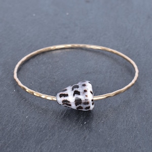 May include: A gold bangle bracelet with a white and black seashell charm.