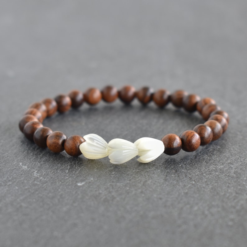 May include: A brown wooden beaded bracelet with three white flower-shaped beads.