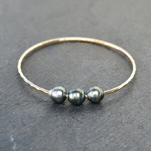 May include: A gold bangle bracelet with three dark gray pearls.