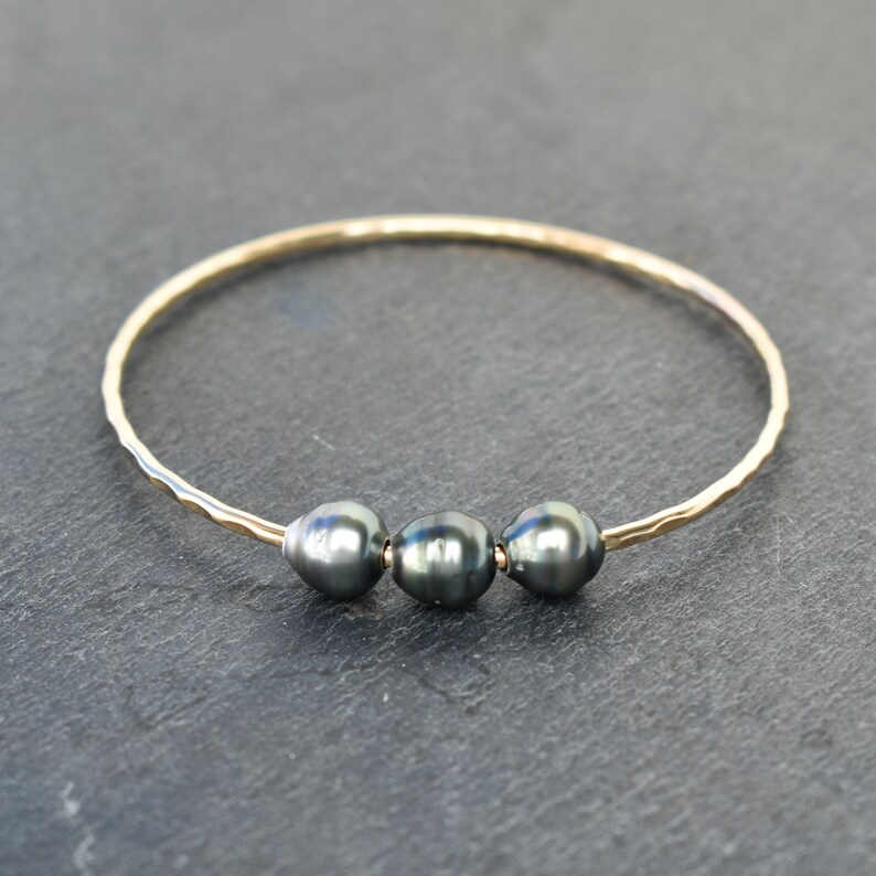 May include: A gold bangle bracelet with three dark gray pearls.