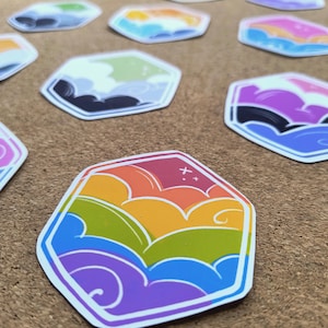 Op de afbeelding: Een verzameling zeshoekige stickers met gestileerde wolkenpatronen in diverse kleurenpaletten, waaronder regenboog-, paarse, blauwe en groene gradiënten, met kleine steraccenten geïntegreerd in de grafische ontwerpen.