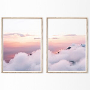 May include: Two framed prints of a pink and purple sunset over a mountain range with clouds. The clouds are white and fluffy, and the sky is a soft pink and purple.