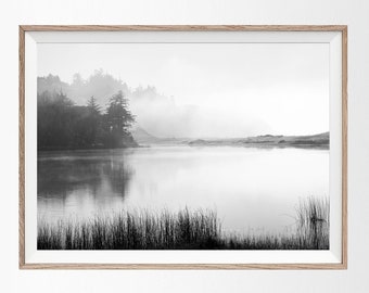 May include: A black and white photograph of a lake with trees and fog in the background. The lake is calm and still, and the trees are reflected in the water.