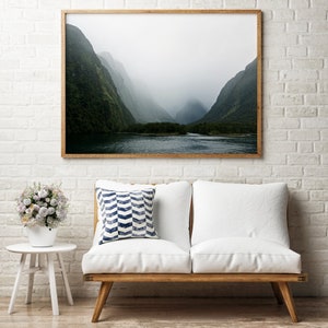 May include: A framed photograph of a misty mountain landscape with a lake in the foreground. The mountains are covered in lush green foliage and the sky is a soft gray.