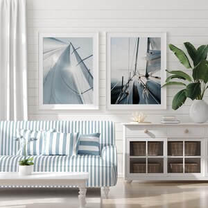 May include: Two framed photographs of a sailboat with white sails against a blue sky and ocean. The photos are hung on a white shiplap wall above a blue and white striped sofa.