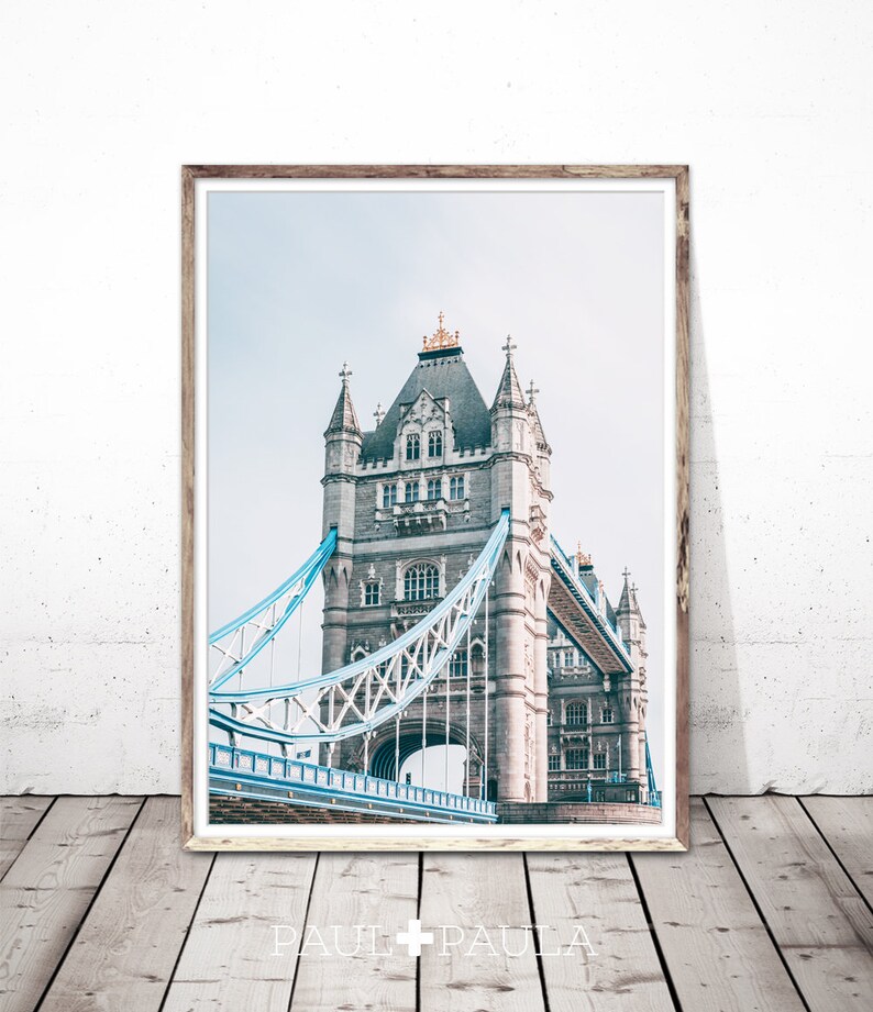 May include: A framed photograph of Tower Bridge in London, England. The bridge is a gray stone structure with blue and white suspension cables. The photo is taken from a low angle, looking up at the bridge.