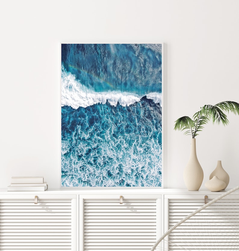 May include: An aerial photograph of a blue ocean with white foamy waves crashing on the surface. The water is a deep blue color and the waves are white and foamy. The photo is taken from a high angle, giving a wide view of the ocean.