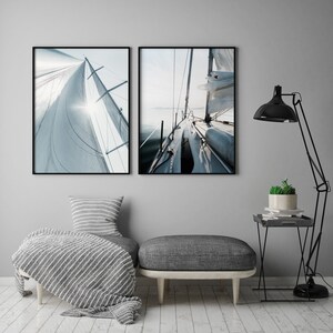May include: Two framed photographs of a sailboat with white sails against a blue sky and water. The first photo shows the sail from the side, while the second photo shows the deck of the boat.